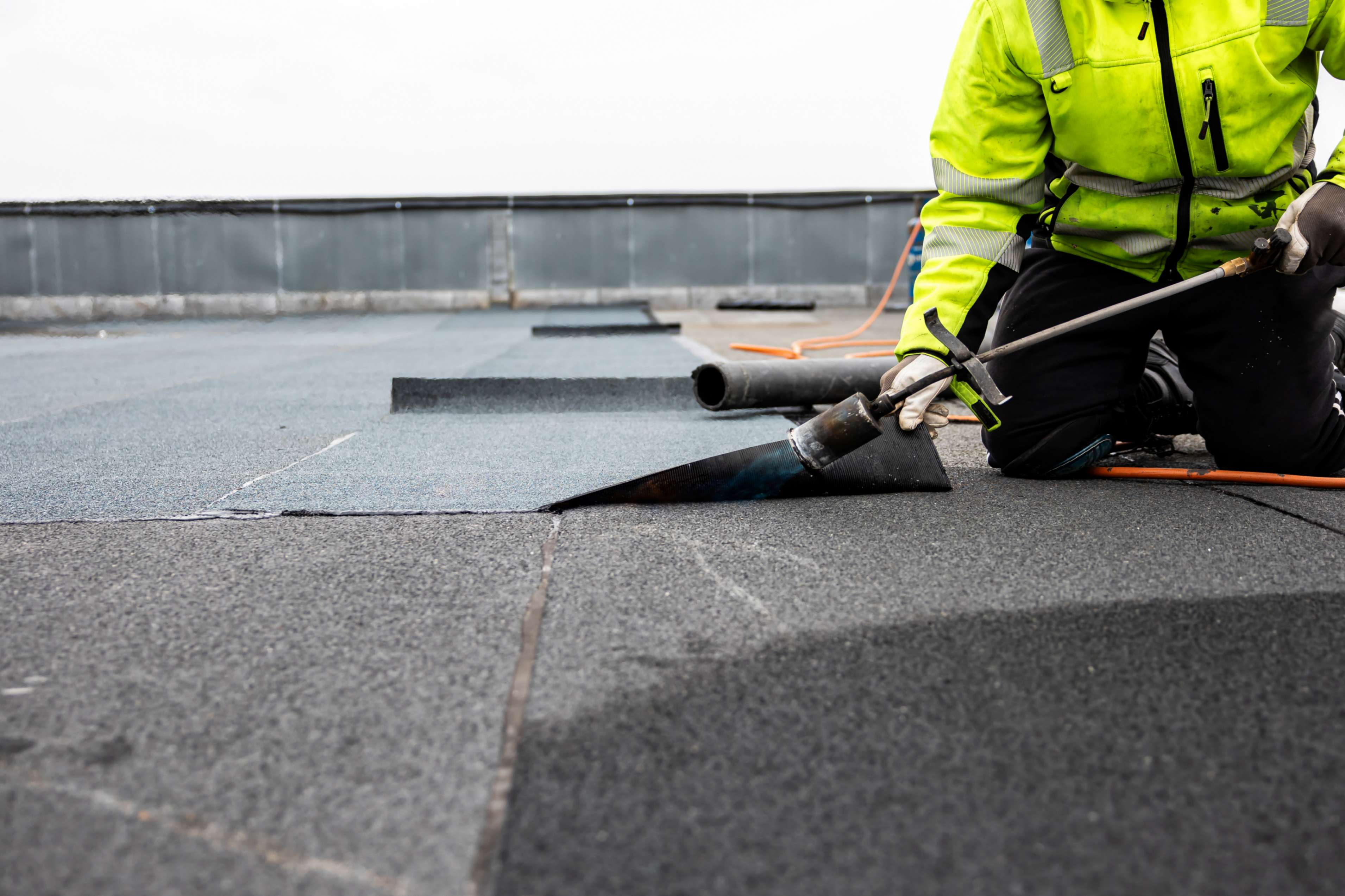 Worker installing waterproof roofing with torch.