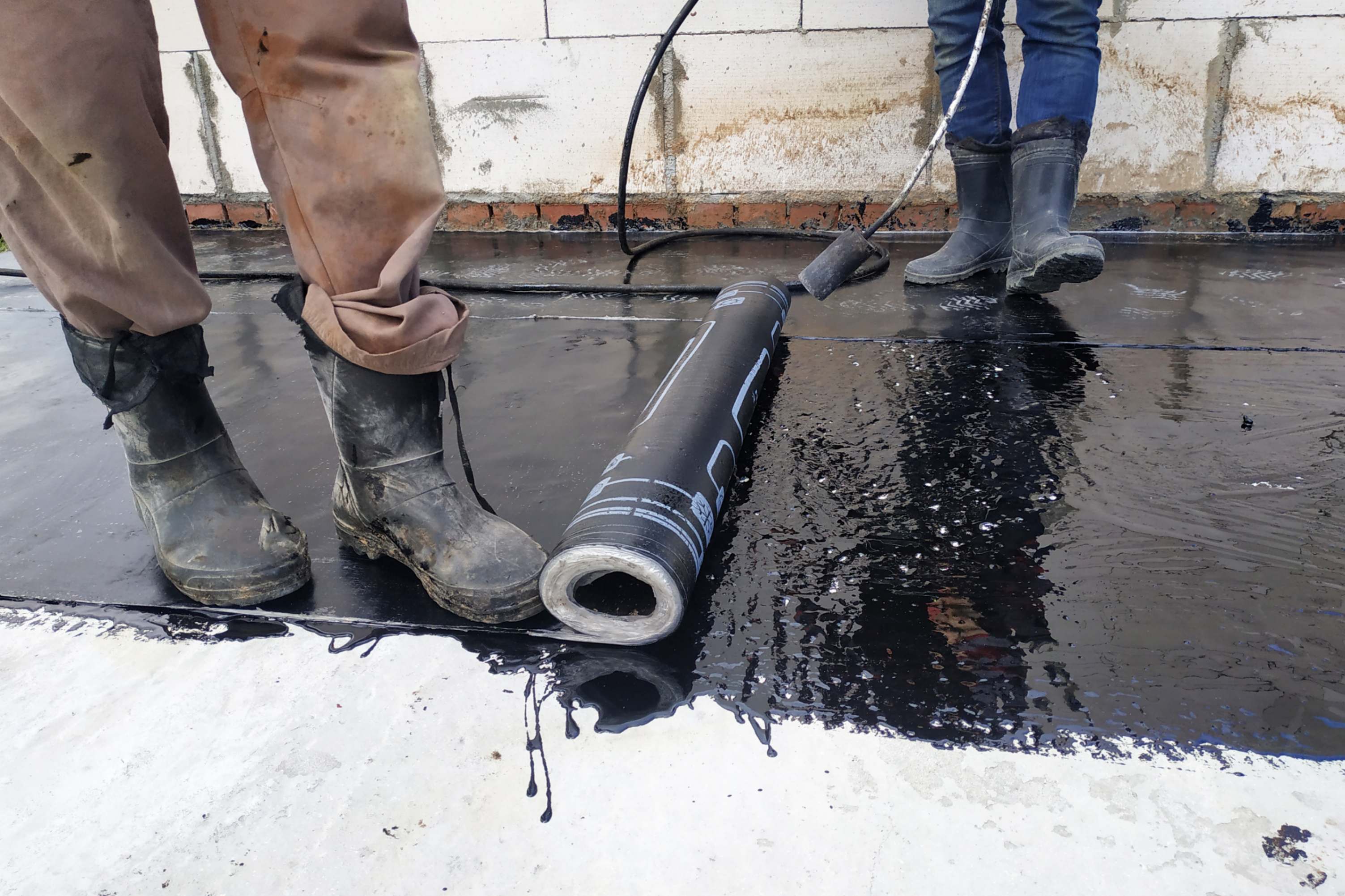 Workers applying waterproofing membrane on floor.