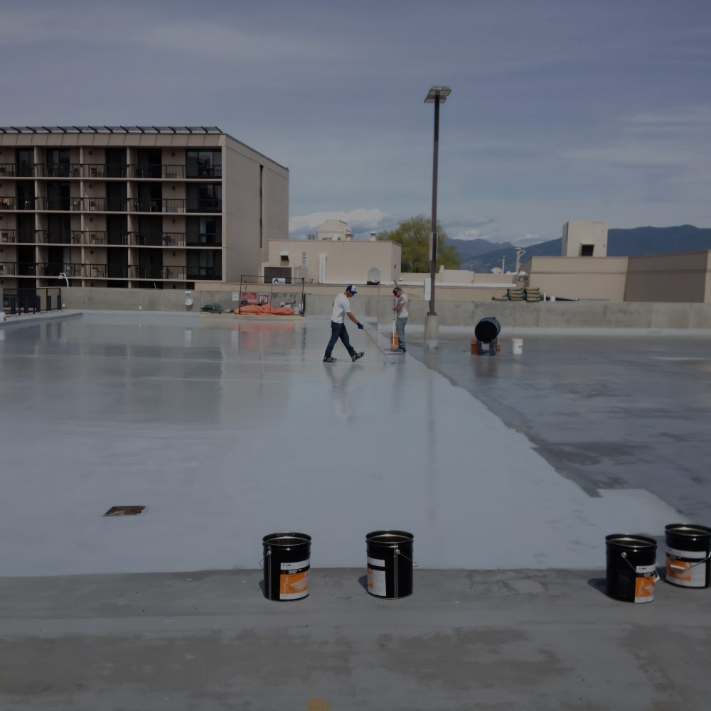 Workers applying coating on rooftop surface.
