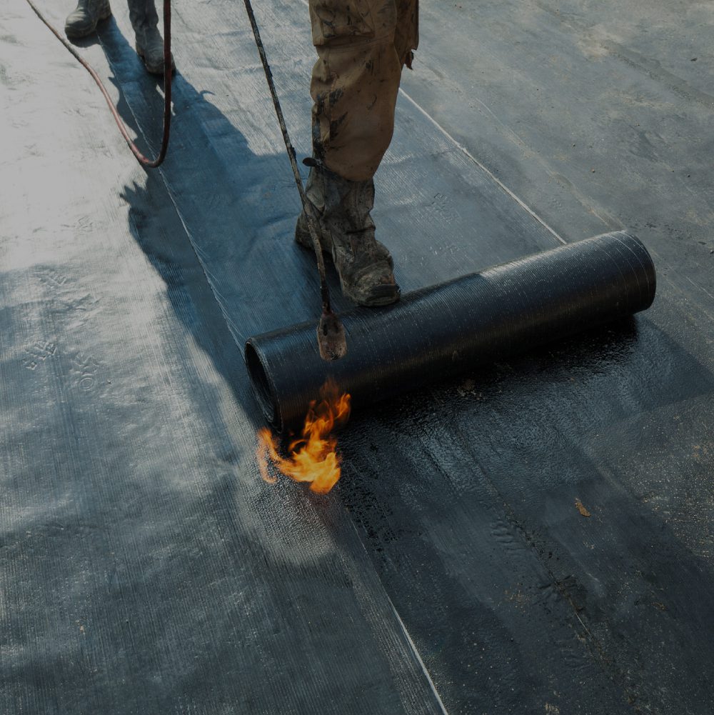 Worker uses a torch to apply roofing material on a flat roof.